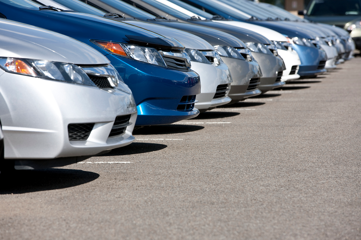 A row of parked cars in various shades of silver and blue, aligned diagonally in a parking lot.