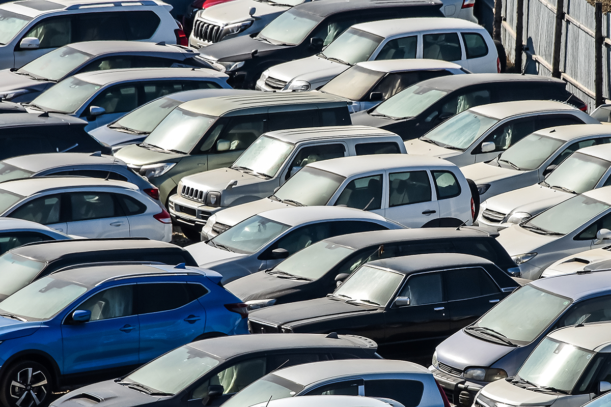 Aerial view of a crowded parking lot filled with various cars, including white, blue, and gray vehicles, tightly parked next to each other.