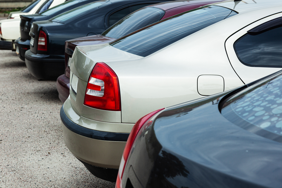 Several parked cars in a row, showing the rear side, with a focus on their taillights, on a light gravel surface.