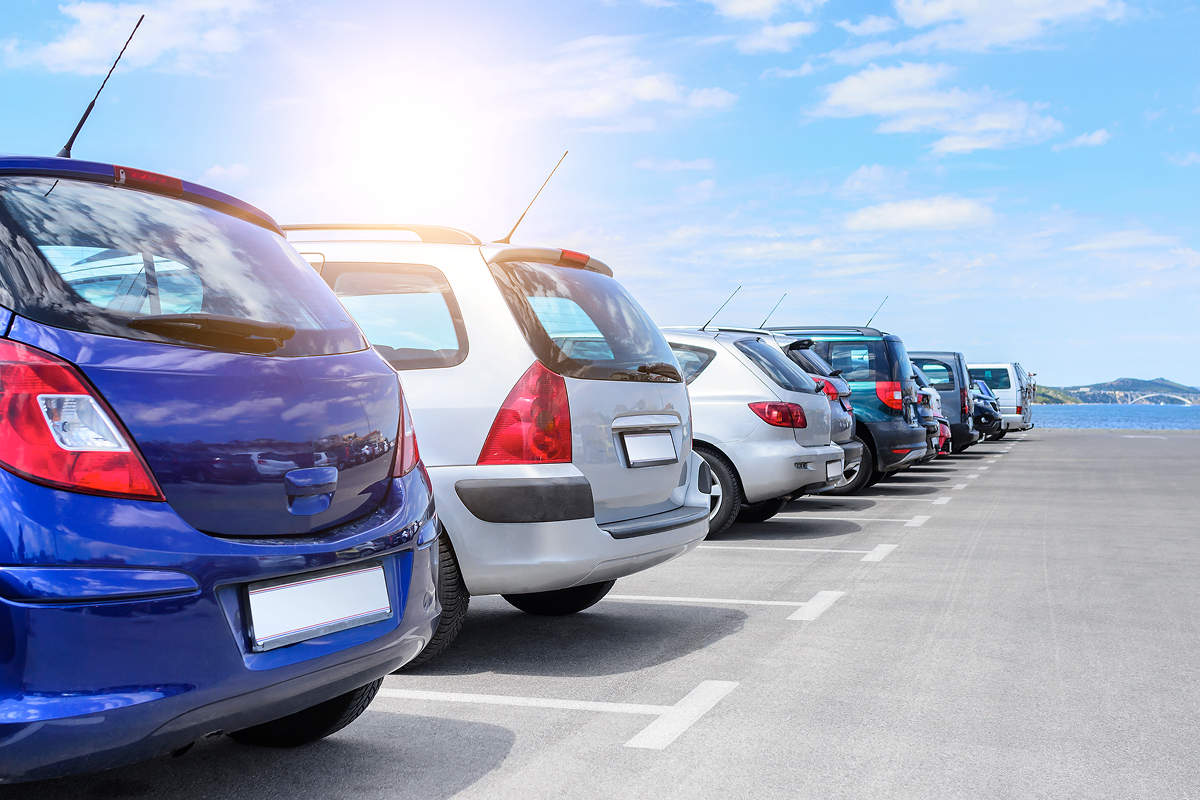Row of parked cars in a parking lot under a clear blue sky, with the sun shining in the background.